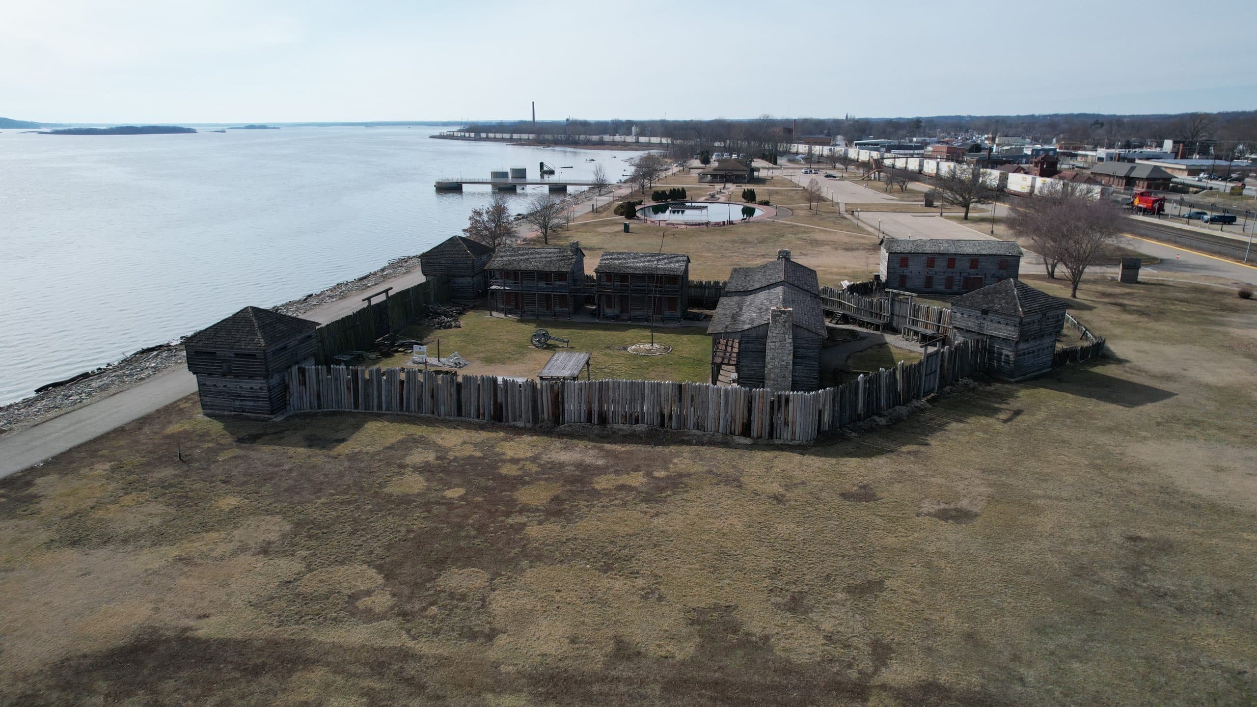 Aerial view of the reconstructed Old Fort Madison beside the Mississippi River, showing the palisade walls, corner blockhouses, barracks, and the open parade ground.
